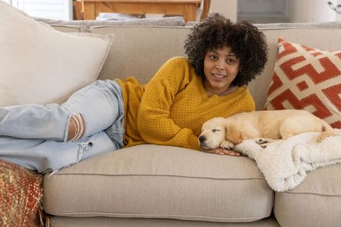African american woman relaxing on sofa with sleeping golden retriever puppy and cozy blanket