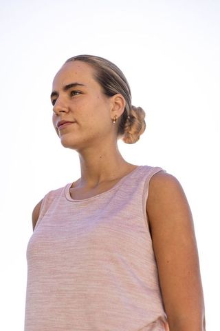 Contemplative young woman standing outdoors in pastel pink top with gold hoop earrings