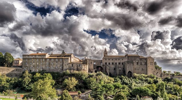 Medieval castle perched on a hill with dramatic clouds overhead showcasing ancient architecture. Ideal for tourism promotions, historical publications, travel brochures, and heritage site documentation.