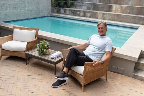Mature man relaxing on wicker chair beside private pool in modern minimal courtyard
