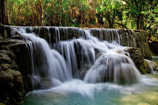 This image depicts a large waterfall cascading over rocky formations surrounded by lush green foliage. The flowing water creates a serene and tranquil atmosphere. Ideal for use in nature tourism promotions, environmental awareness campaigns, relaxation and meditation visuals, and outdoor adventure blogs.