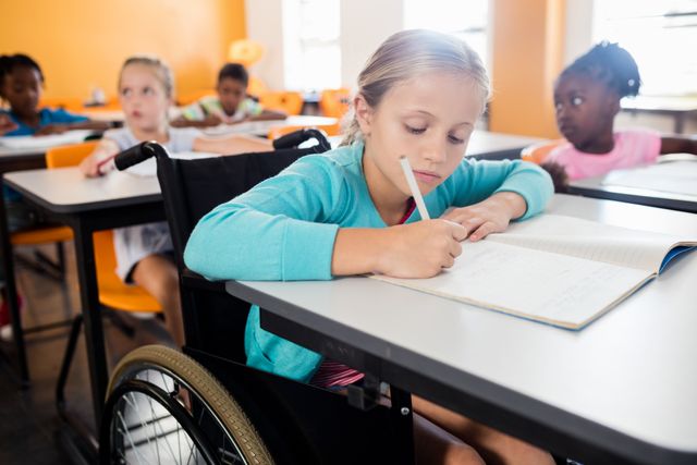Portrait of a cute pupil in wheel chair working at desk in classroom