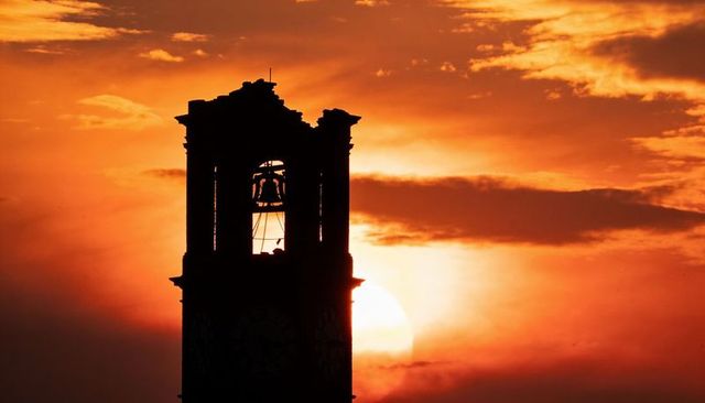 Silhouetting historic bell tower at sunset with clock face and hanging bells