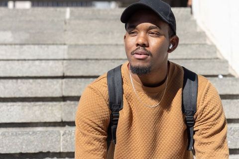 African american commuter sitting on stairs wearing earbuds and backpack in sunlit urban