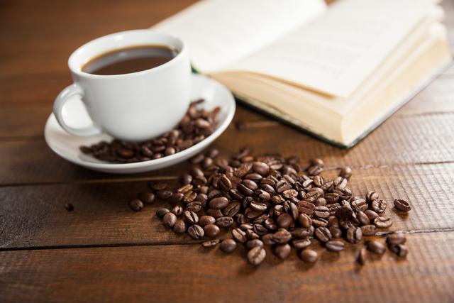 Cup of coffee with coffee beans and book on wooden table
