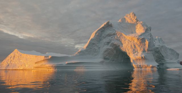 Sunset casts warm light on a massive iceberg floating in Disko Bay near Ilulissat, Greenland. Captured on July 24, 2015, this image highlights the dramatic impacts of climate change and sea level rise. Ideal for illustrating environmental changes, global warming discussions, and natural beauty in arctic regions.