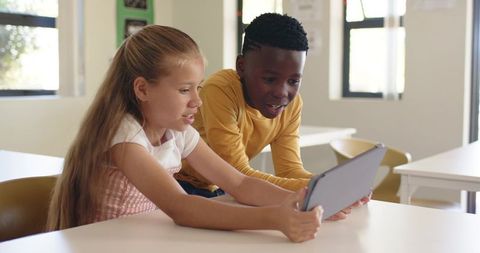 Black boy and white girl collaborating on tablet in bright classroom learning together