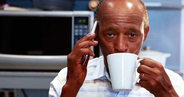 Older man drinking coffee and talking on phone in kitchen - Download Free Stock Images Pikwizard.com