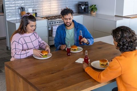 Three friends sharing burgers and drinks at modern kitchen island, casual home meal