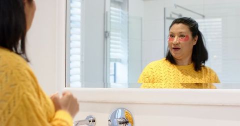 Senior woman practicing self-care with gel eye patches in modern bathroom