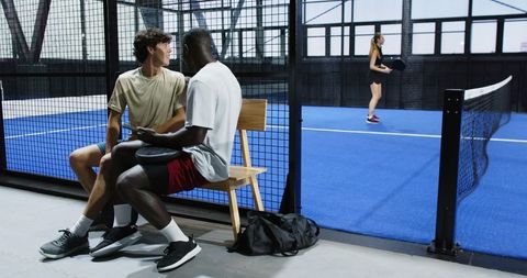 Teammates Sitting with Padel Rackets on Indoor Court