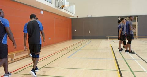 School basketball players standing on sideline in gym wearing blue jerseys and knee pads