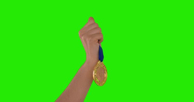 A Caucasian hand is raised, holding a gold medal against a green screen background, with copy space. It symbolizes achievement and success in a competitive event or sport.