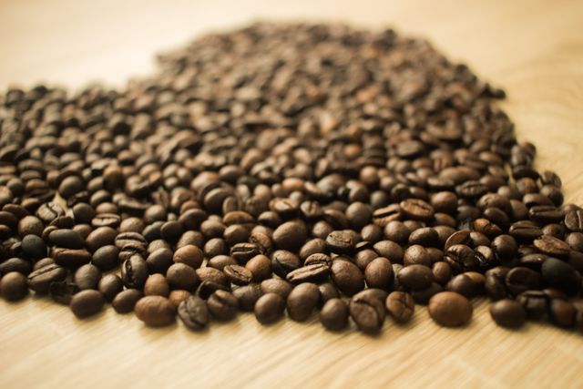 Close-up of coffee beans arranged in heart shape on wooden surface conveys love for coffee. Ideal for use in coffee shop promotions, caffeine-related advertisements, blogs about coffee culture, and designing menu visuals. Emphasizes warm, inviting tones perfect for lifestyle or culinary themes.