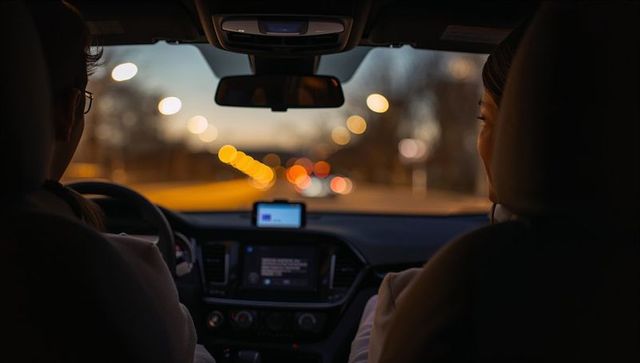 Couple driving at dusk using smartphone navigation inside car with warm bokeh lights
