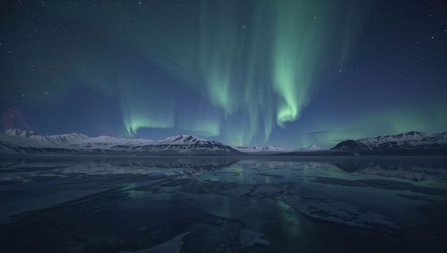 Aurora borealis illuminating icy night over mountain lake