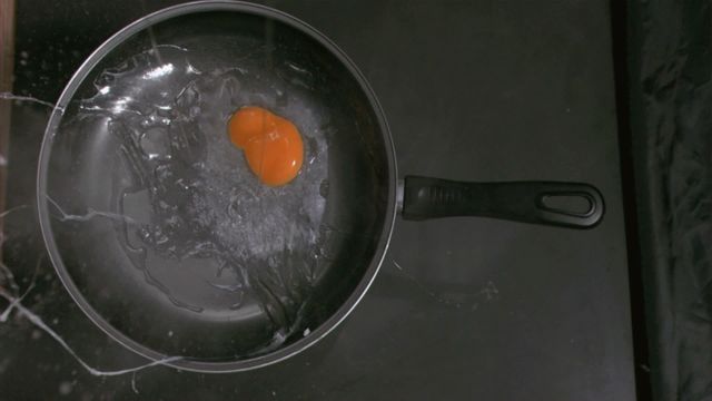 This video captures an egg falling into a pan in super slow motion, splashing its yolk across the surface. Ideal for use in cooking tutorials, food preparation guides, cleaning product advertisements, or educational content about kitchen safety and food handling.