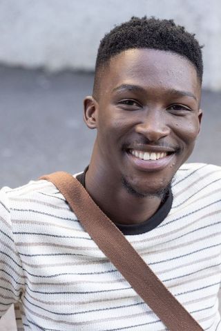 Young man smiling in striped knit sweater with brown crossbody bag urban headshot