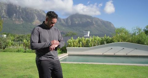 African american man checking smartwatch poolside in backyard with mountain view