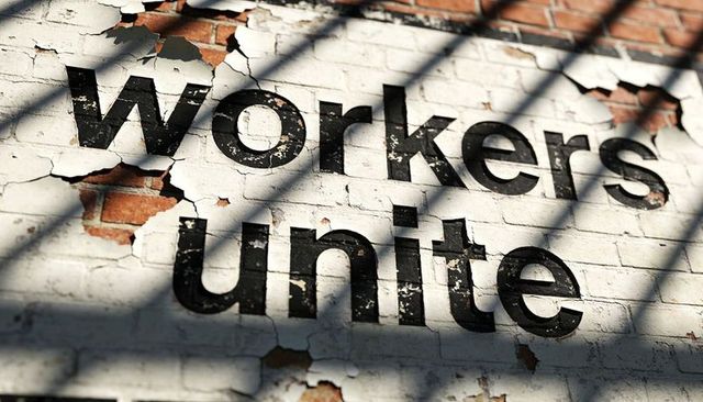 Workers unite mural with peeling paint on brick wall with diagonal shadows, weathered