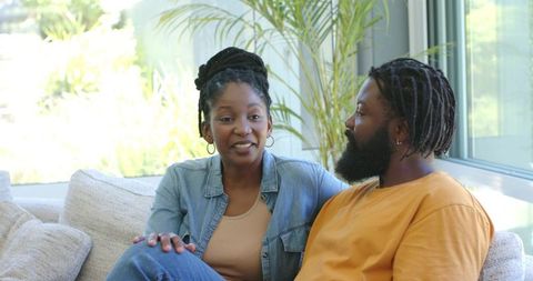 Sunlit couple sharing relaxed conversation on cozy modern sofa near window with indoor plants