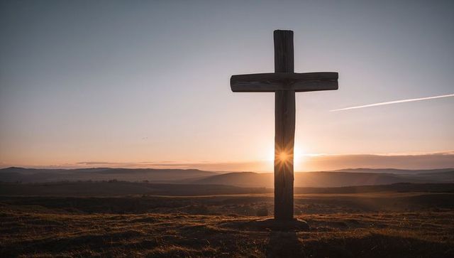 Weathered wooden cross standing on hill at sunrise with sunburst over rolling moors