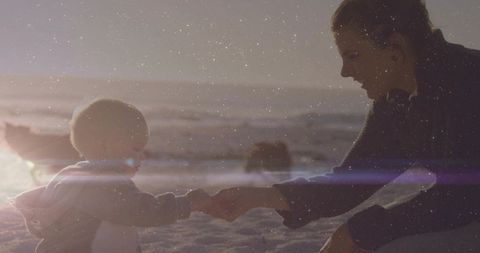 Backlit mother and baby holding hands on sunlit beach with lens flare and silhouette