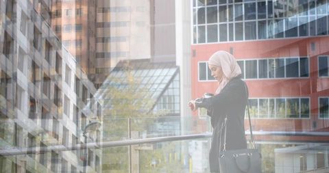 Asian woman wearing hijab checking time on smartwatch in urban landscape