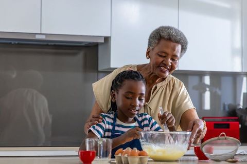African grandmother guiding girl baking at kitchen island, intergenerational mentoring