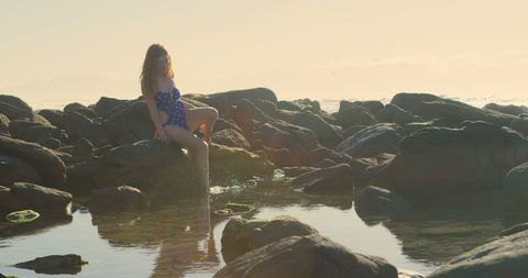 Woman Relaxing on Seaside Rocks at Sunset with Tranquil View