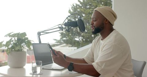 Recording podcast from home desk with boom microphone, laptop and tablet