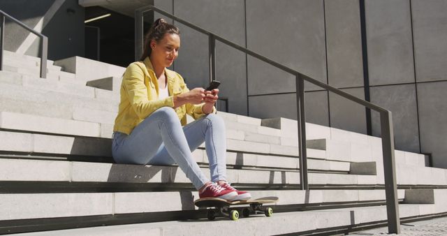 Woman casually sitting on stairs with skateboard next to her, texting on smartphone in urban environment. Ideal for themes related to youth, technology, urban lifestyle, modern communication, relaxation, and skateboarding culture.