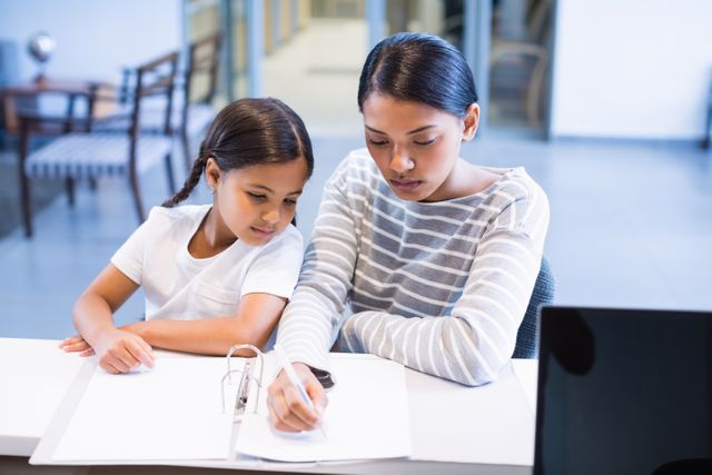 Mother and daughter sitting at a counter in a hospital, focusing on completing paperwork. Ideal for use in healthcare, family support, medical assistance, and patient care contexts.