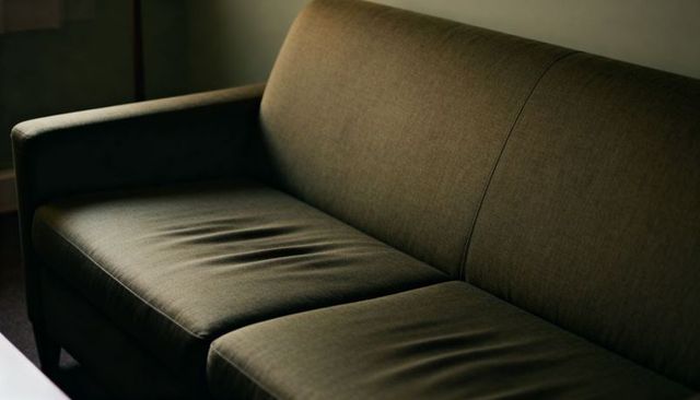 Olive sofa showing sagging cushions and stitched seams in warm moody lounge light