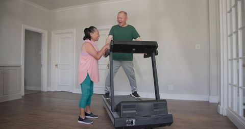 Elderly couple exercising on treadmill at home sharing joyful moment