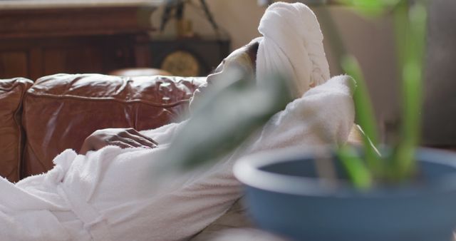 Woman resting on a couch wearing a bathrobe and towel on her head, suggesting a peaceful and relaxing atmosphere at home. Useful for wellness blogs, spa advertisements, relaxation product promotions, and lifestyle articles focusing on self-care and tranquility.