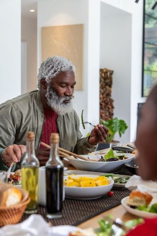 Senior african american man enjoying family dinner inspecting salad with chopsticks in modern home