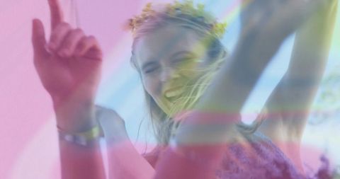 Dancing blonde woman wearing floral crown and wristband at outdoor festival with pastel light