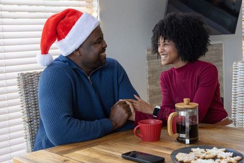 African american couple sharing cozy holiday coffee and cookies, smiling and holding hands