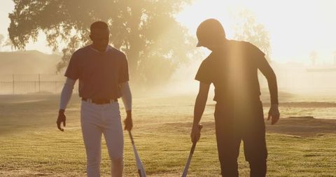 Diverse Teammates Practicing Baseball at Sunset Backlit Field Holding Bats and Helmet