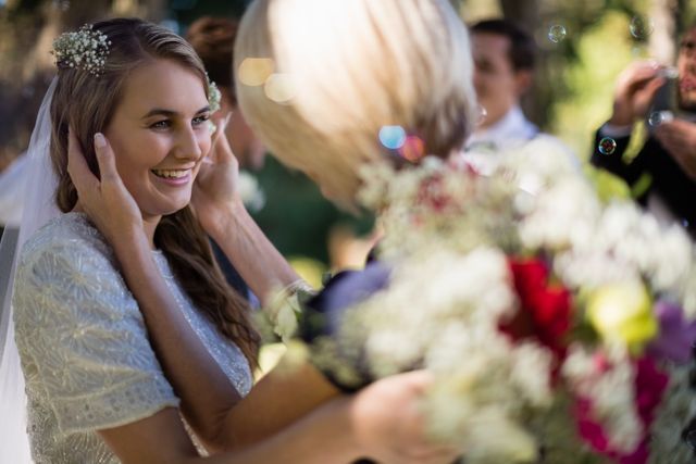 Bride smiling and interacting with guests in a park setting during a wedding ceremony. Ideal for use in wedding planning materials, bridal magazines, and event promotion. Captures the joy and connection of a wedding day.