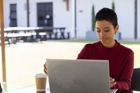 African american woman working on laptop outdoors on campus courtyard with coffee