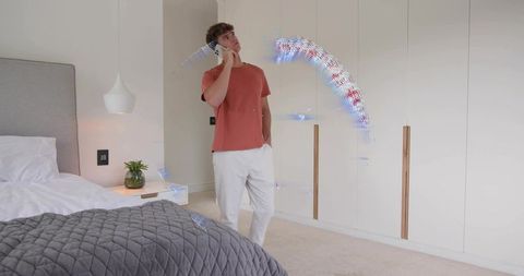 Young man talking on smartphone in modern bedroom with digital light trails and calm decor