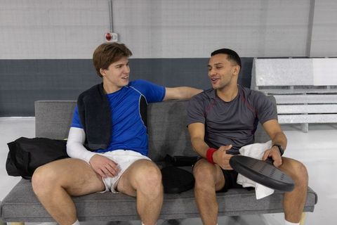 Teammates chatting and relaxing after pickleball match on bench with paddles and towels