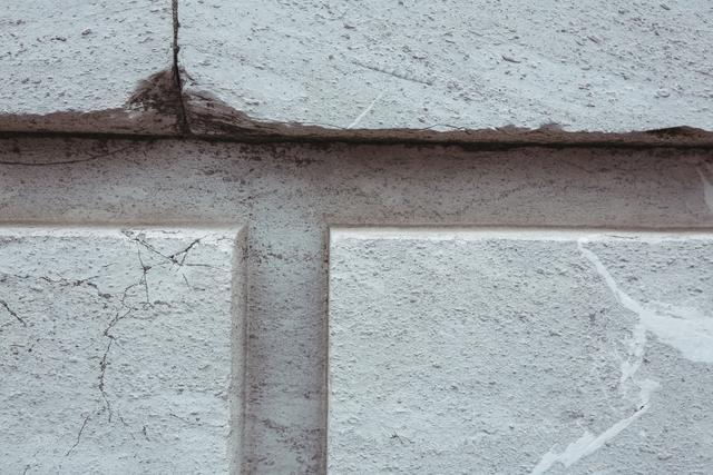 This close-up of a white painted stone wall with visible cracks and texture is ideal for use in architectural presentations, construction materials catalogs, or as a background in design projects. The detailed texture and weathered appearance can add a rustic or industrial feel to various creative works.
