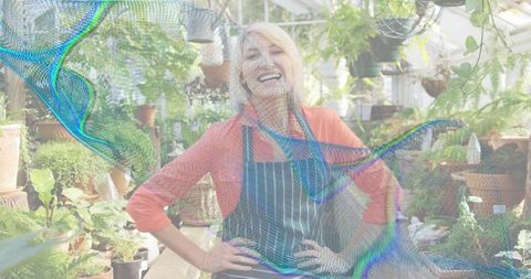 Smiling senior gardener tending lush greenhouse plants wearing striped apron in glasshouse