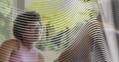 Young woman wearing glasses sitting behind ribbed glass at cafe, contemplative daylight