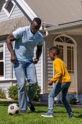 African american father playing soccer with son on front lawn family outdoor bonding