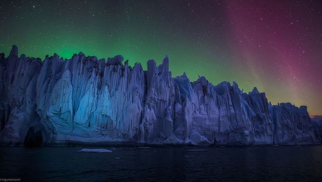 Aurora-lit Glacier Wall Rising from Dark Arctic Sea under Starry Night Sky