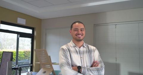 Asian professional standing arms crossed smiling in modern sunlit office workspace